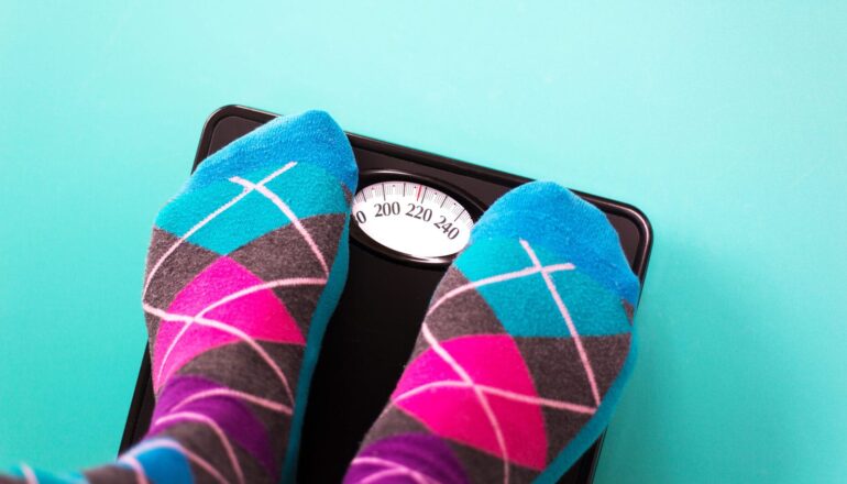 A person wearing colorful argyle socks stands on a bathroom scale on a blue background.