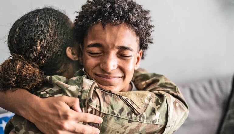 A teen hugs his mother, who is wearing a military uniform.