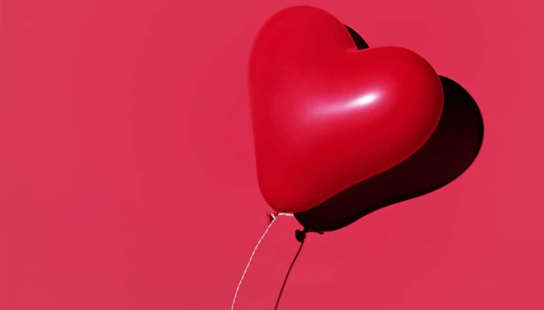 A red balloon in the shape of a heart floats in front of a red background.