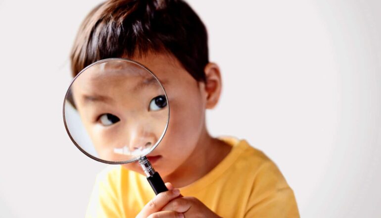A preschool-age boy looks through a magnifying glass.