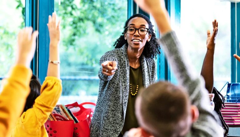 A teacher calls on students raising their hands in a classroom.