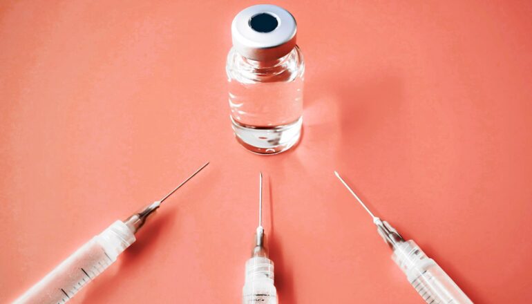 Three syringes surround a vial of vaccine.