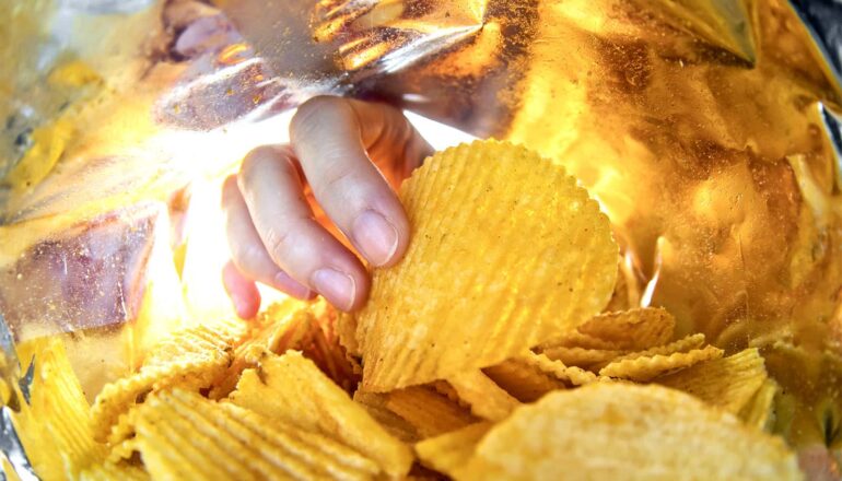 A hand reaches into a potato chip bag.