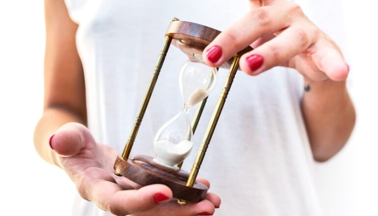 A woman holds a small hour glass.