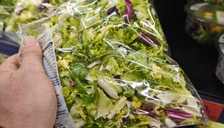 A person holds a bag of lettuce at the grocery store.