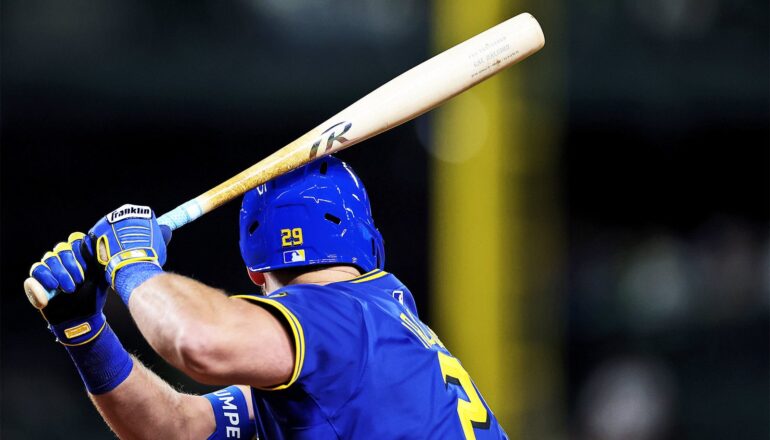 A baseball player holds up a torpedo bat while waiting to swing at an oncoming pitch.
