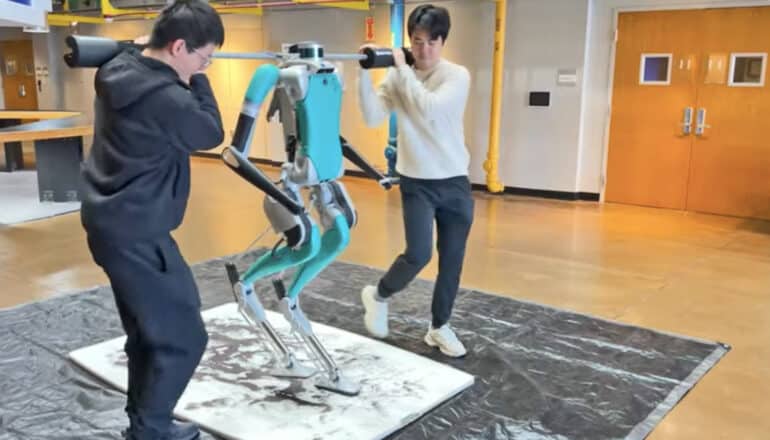 Two researchers help a robot walk across a slippery floor.
