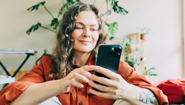 A woman smiles while scrolling on her phone.