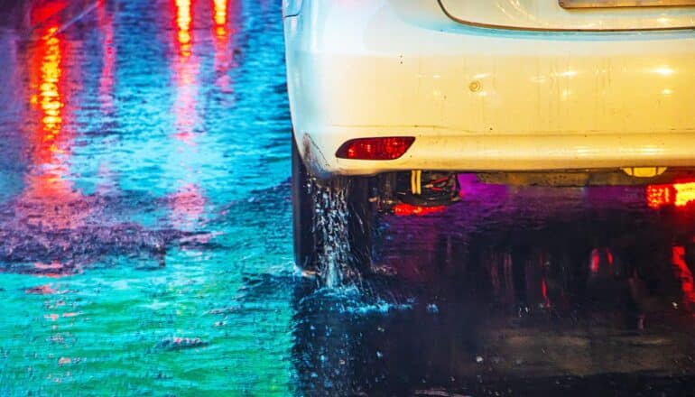 A car drives on a raining street reflecting lights.