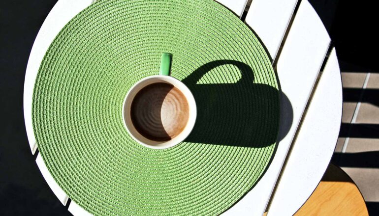 A cup of coffee with creamer in it sits on a round table.