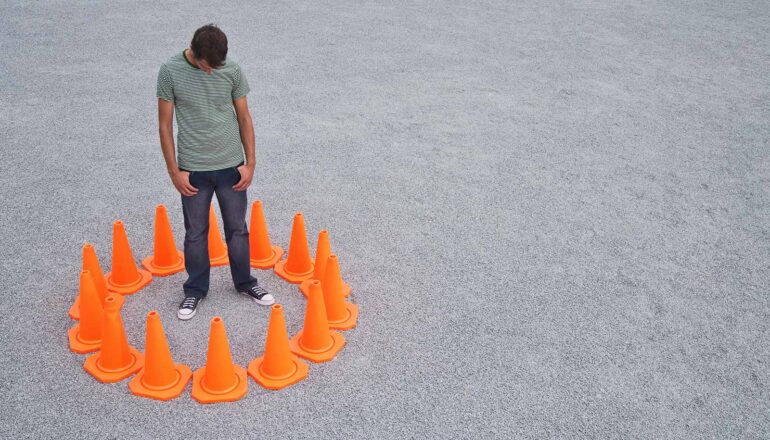 A man stands inside a ring of orange traffic cones.